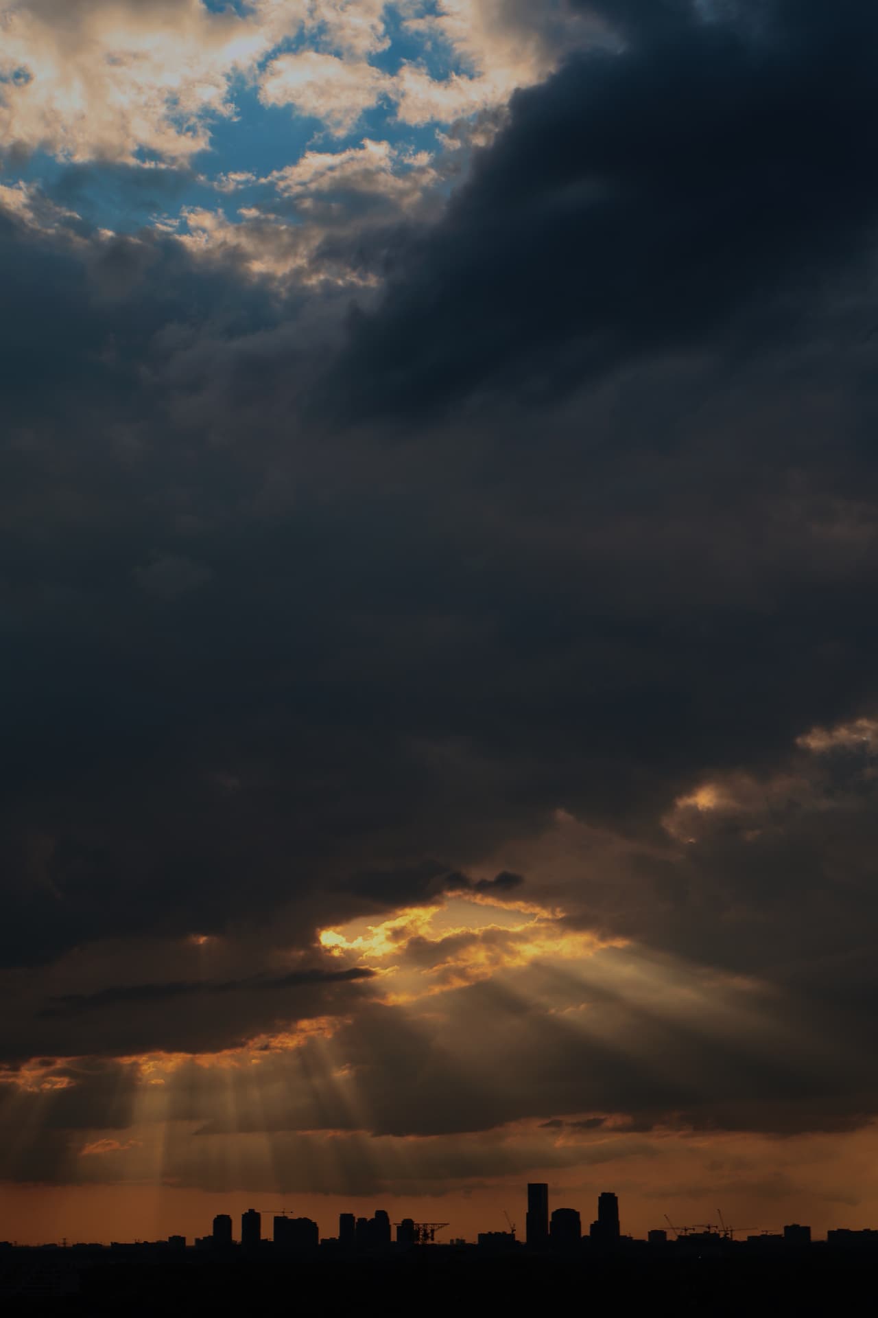 Crepuscular rays breaking through heavy storm clouds above a city skyline at sunset