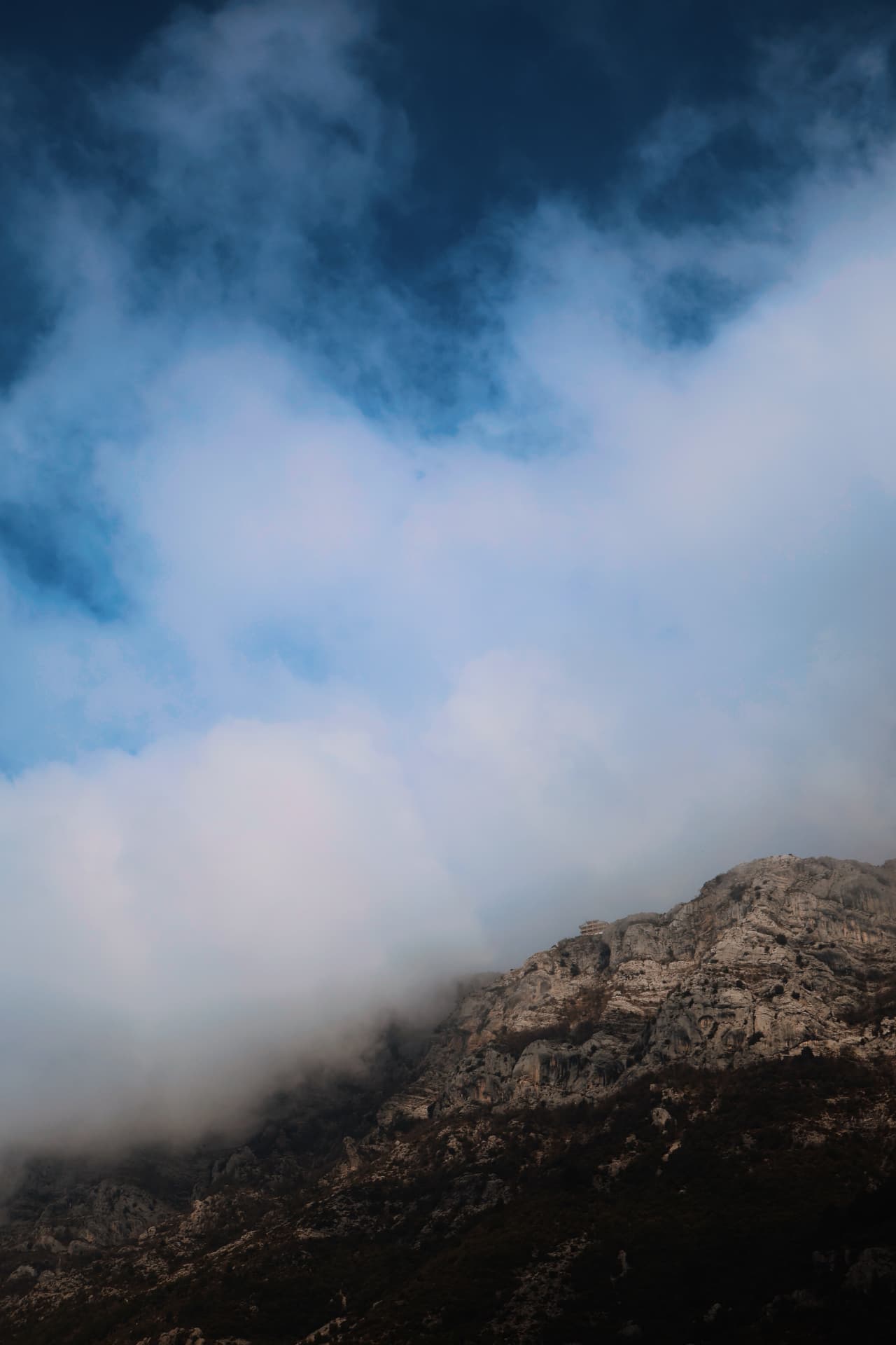 Low cloud pouring over a rocky mountain cliff beneath a deep blue sky