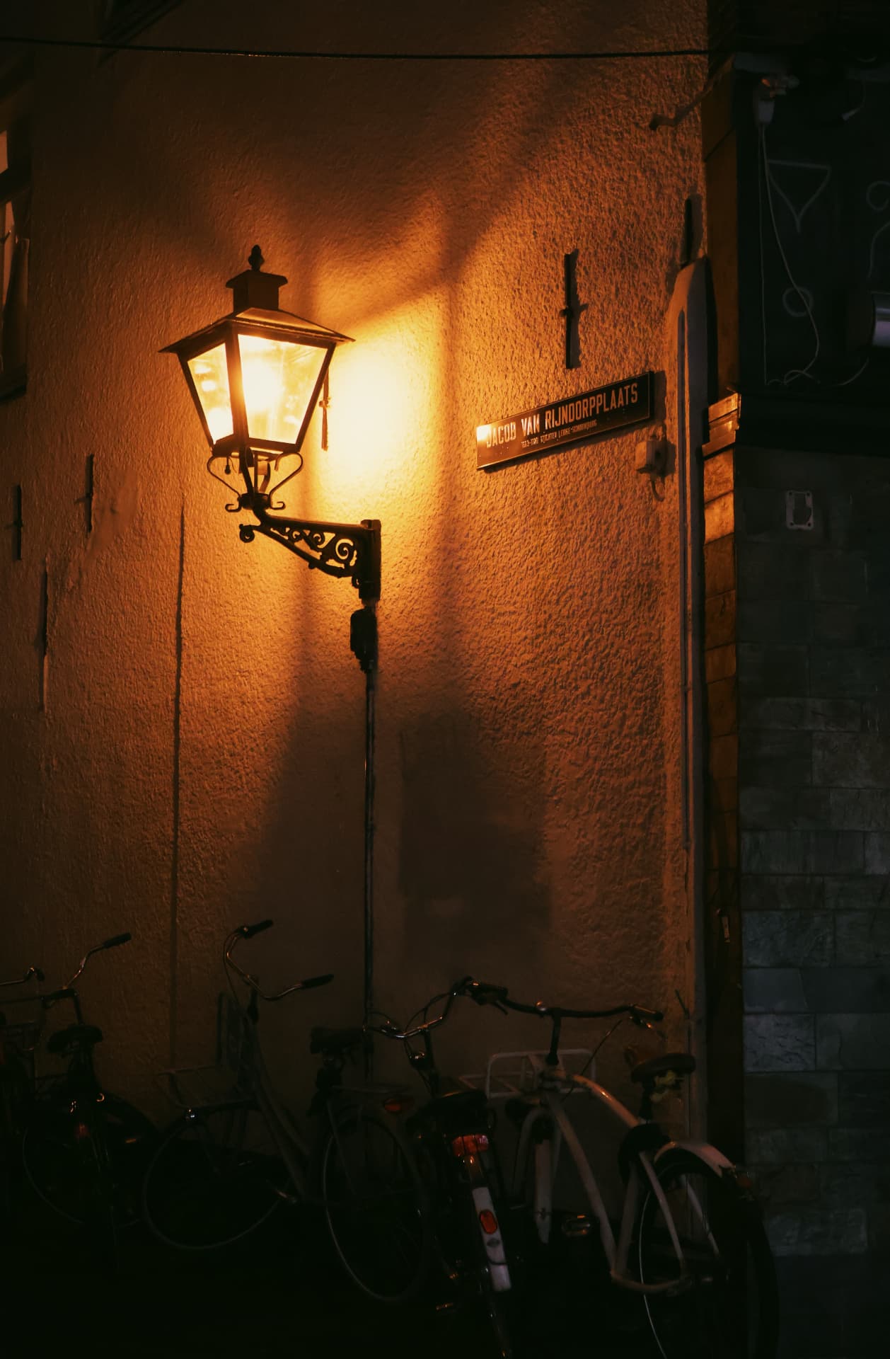 A warm street lamp glowing above parked bicycles beside a street sign at night