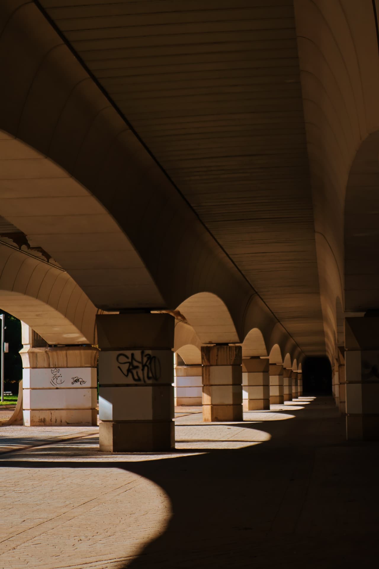 Repeating concrete arches beneath a bridge casting pools of warm light and deep shadow