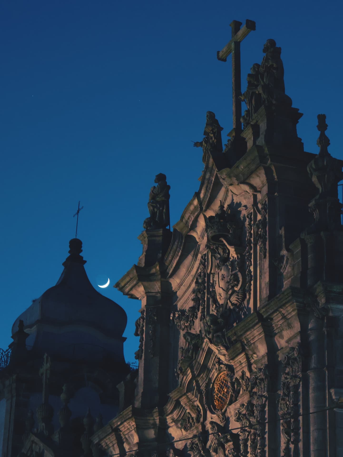 An ornate baroque church facade with a crescent moon in a deep blue evening sky