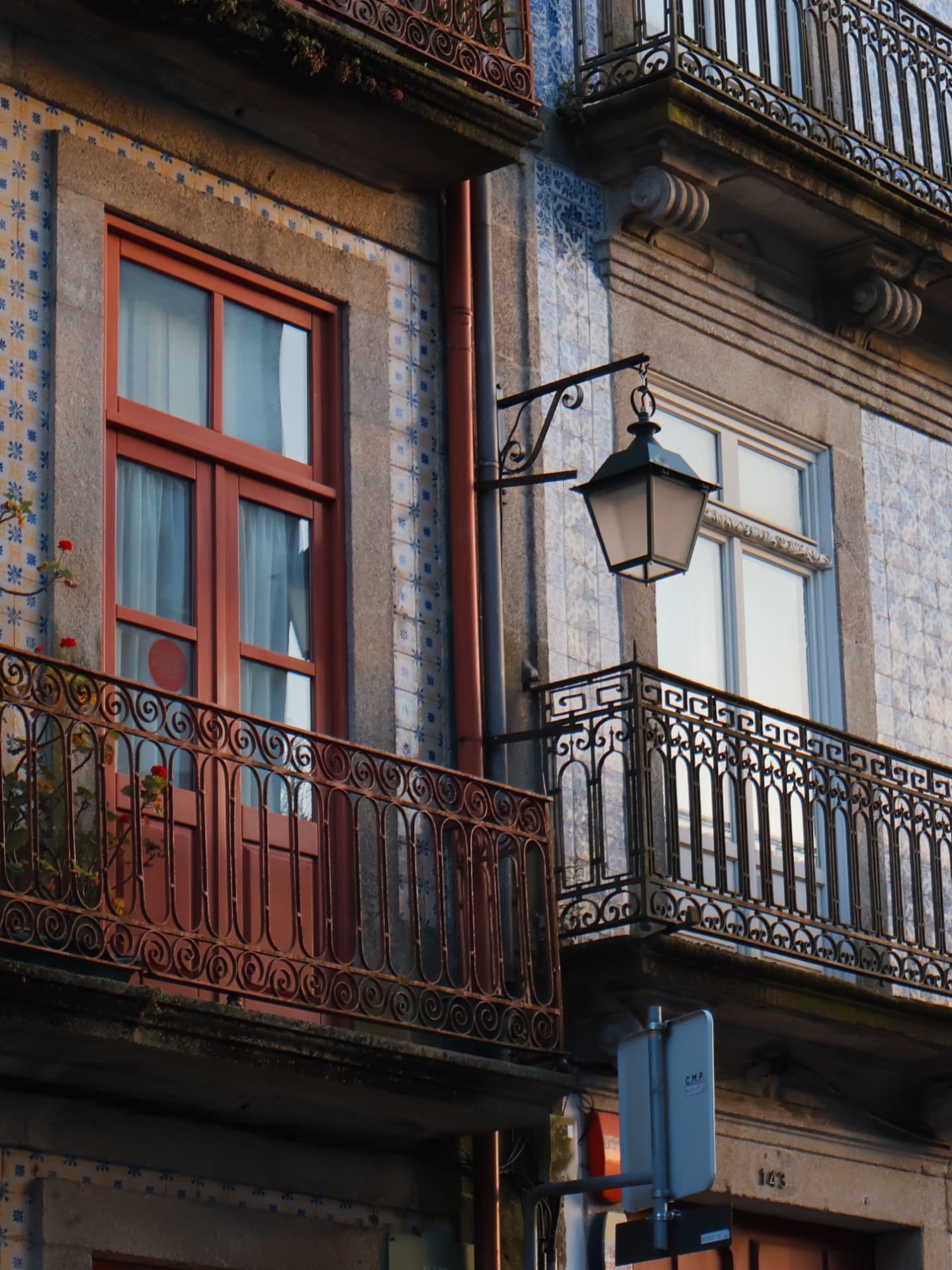 Wrought-iron balconies and a street lamp against azulejo-tiled facades in warm light