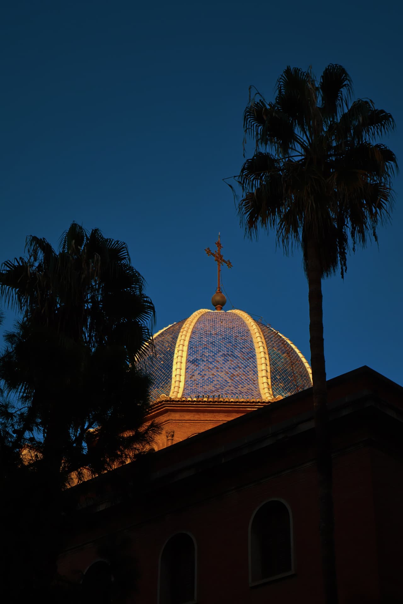 A tiled church dome glowing between palm silhouettes at dusk
