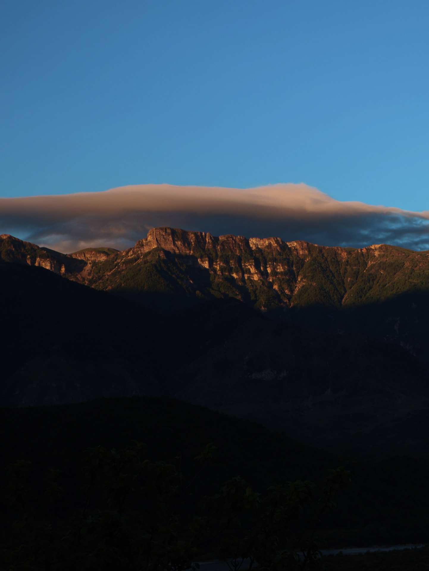 The last warm light striking a mountain ridge beneath a long lenticular cloud