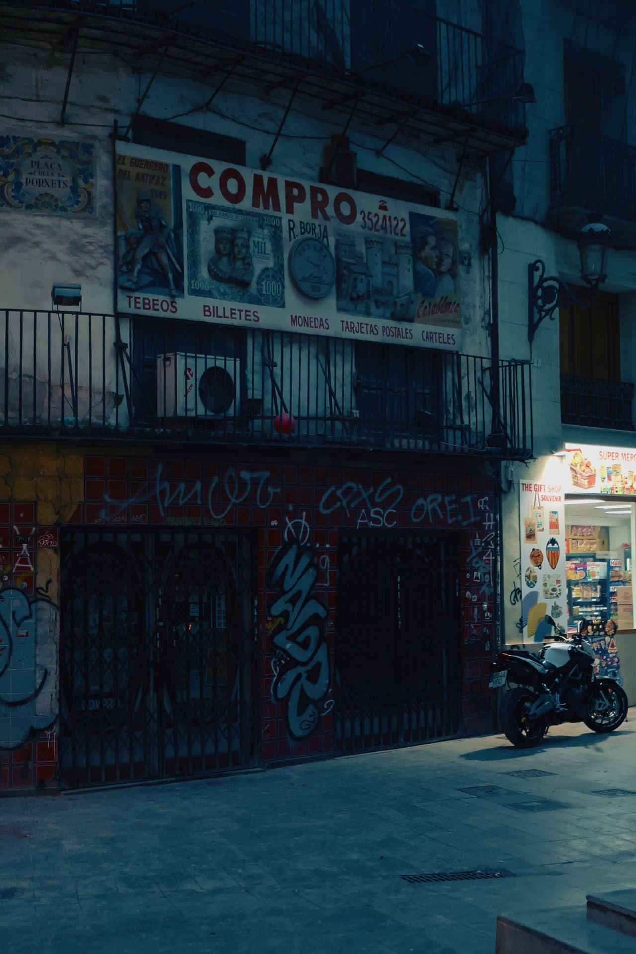 A shuttered storefront with a vintage sign and graffiti under deep blue night light