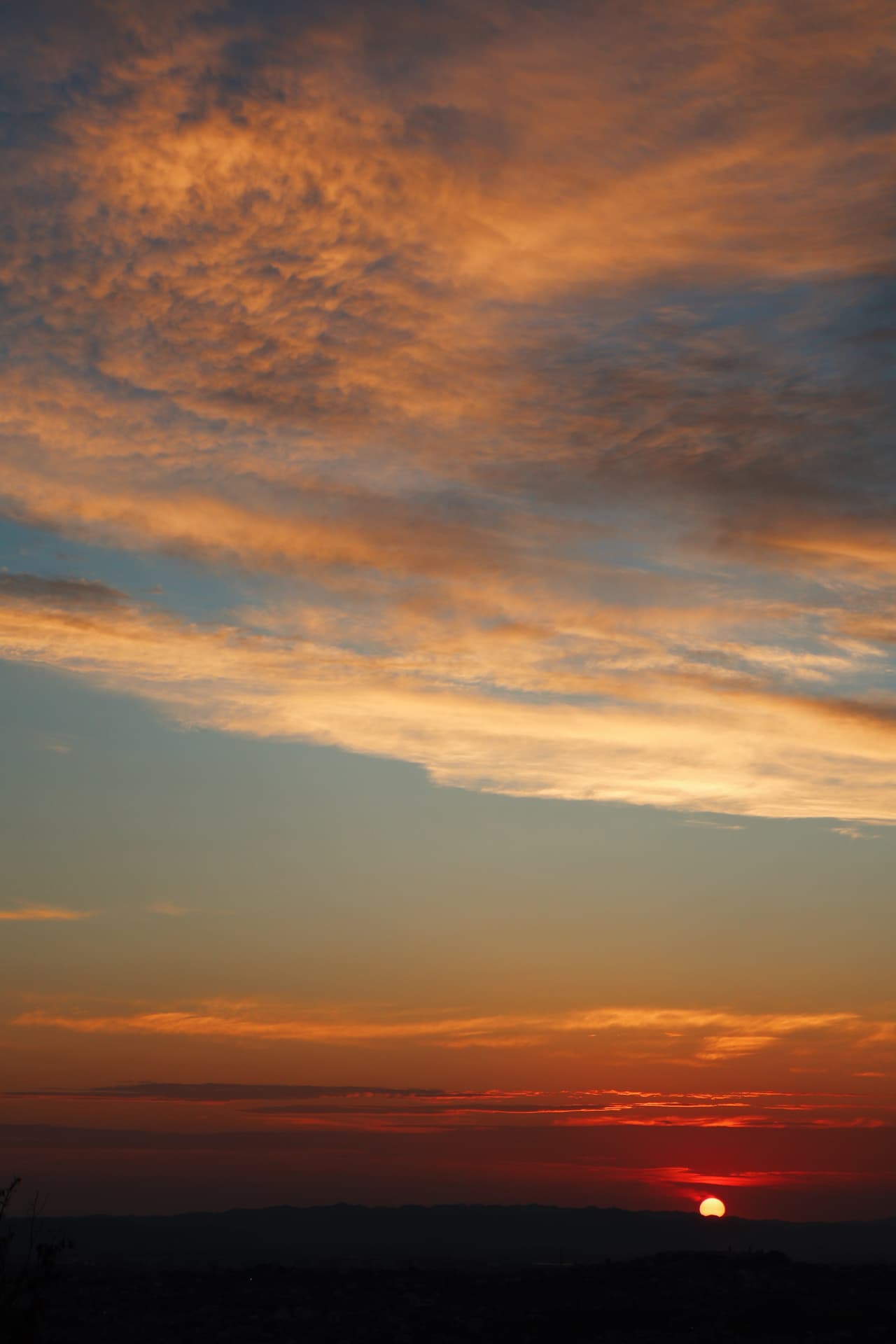 The sun touching the horizon beneath a sky of orange ember clouds
