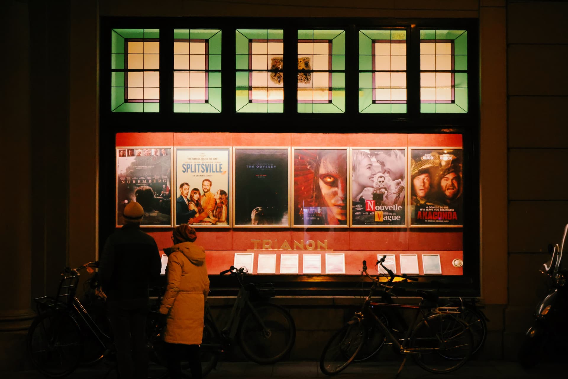 A couple studying glowing cinema posters outside a theatre at night